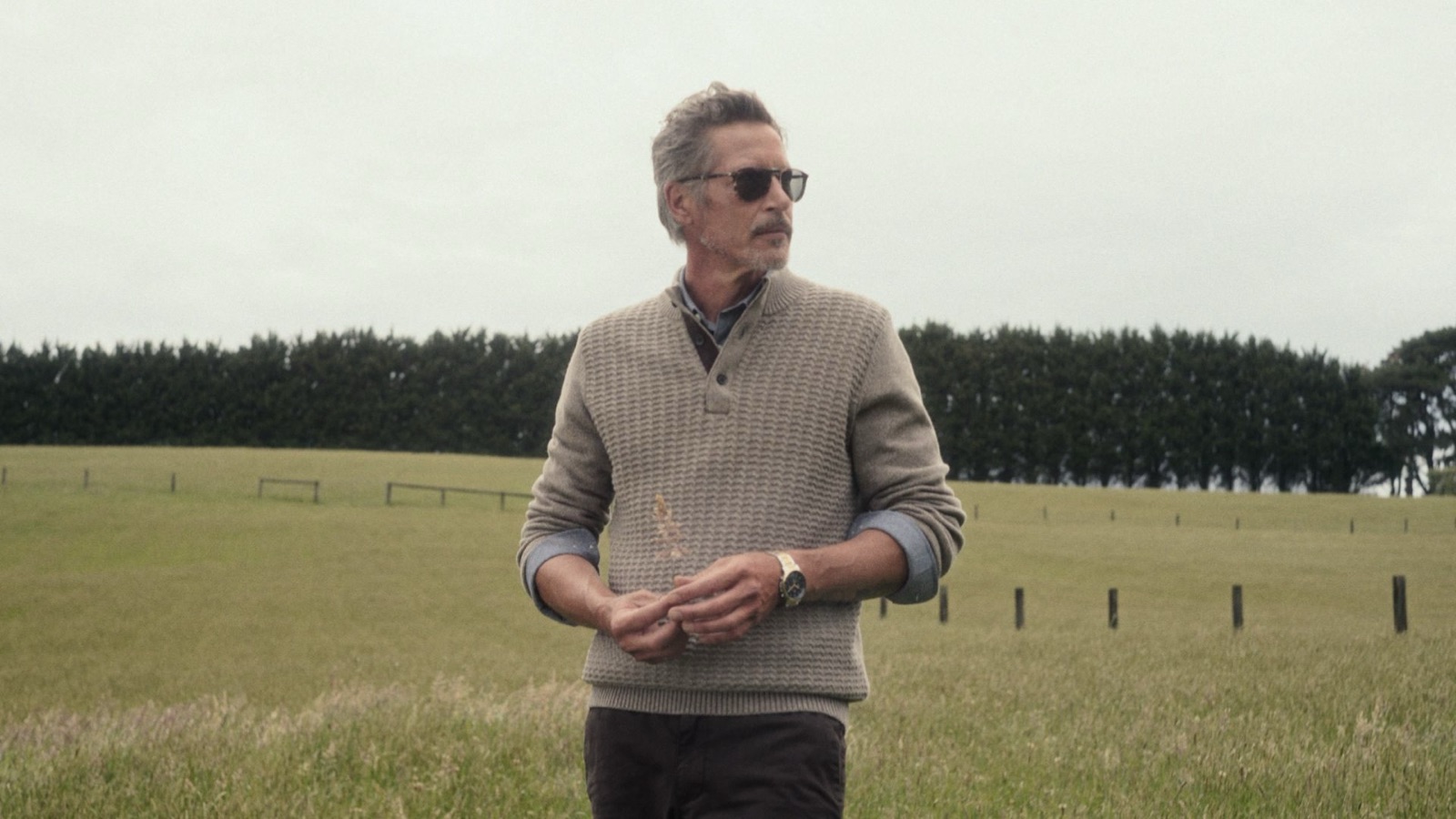 A man in a textured knit and sunglasses standing in an open paddock