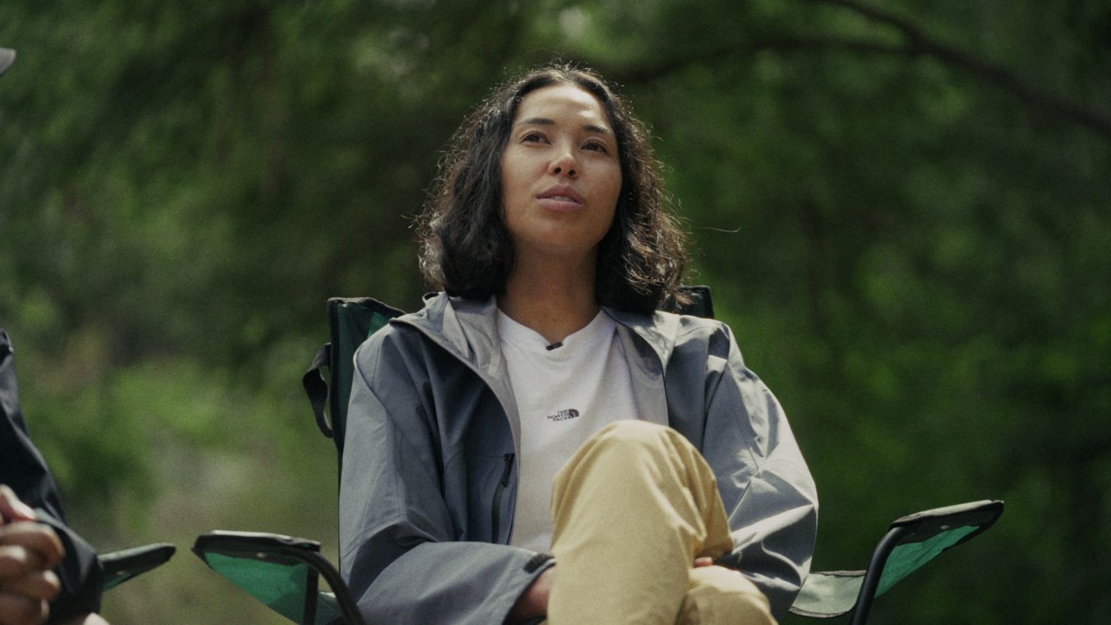 A hiker seated in a camp chair in the bush, looking up