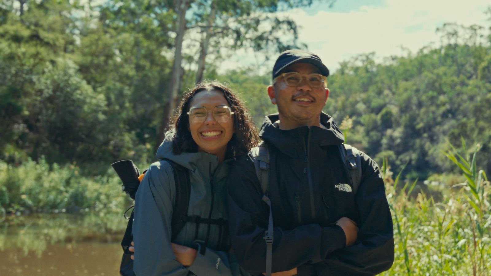 Two hikers smiling together beside a pond