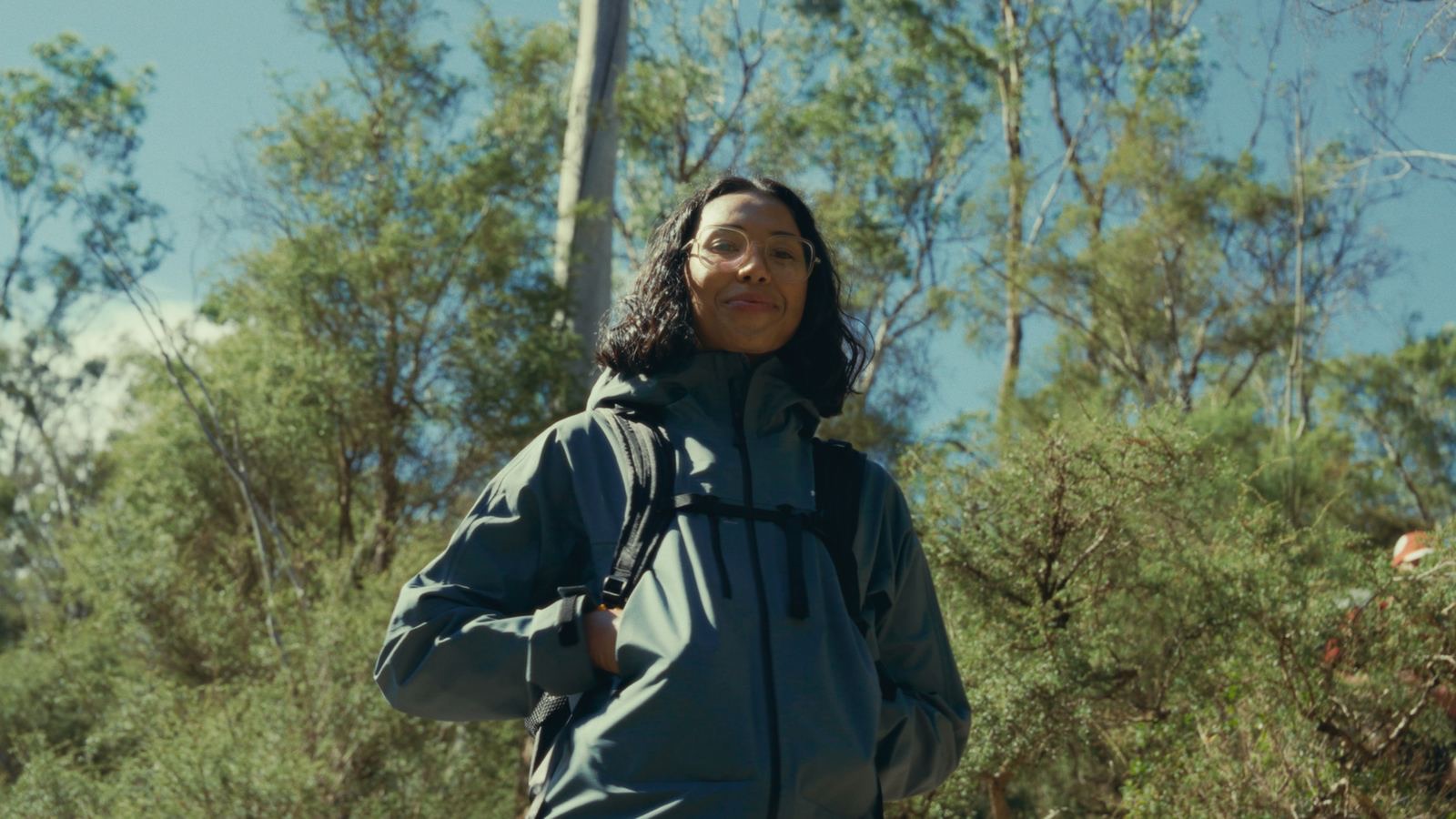A hiker in a teal shell jacket in low scrub