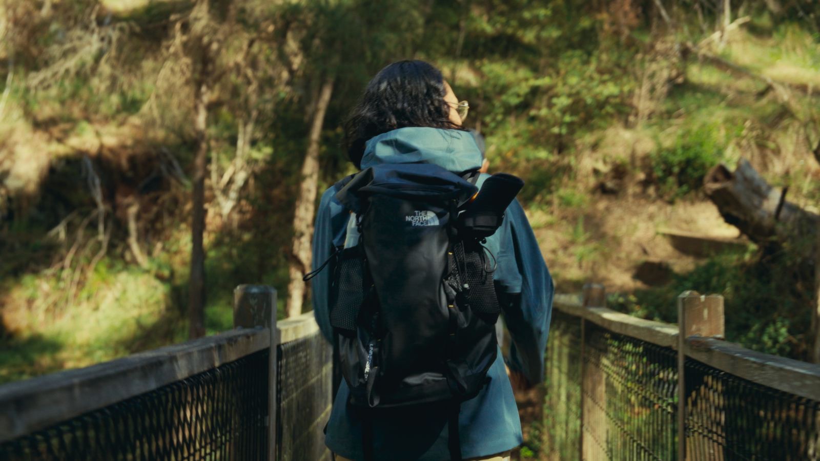 A hiker crossing a wooden bridge, daypack on