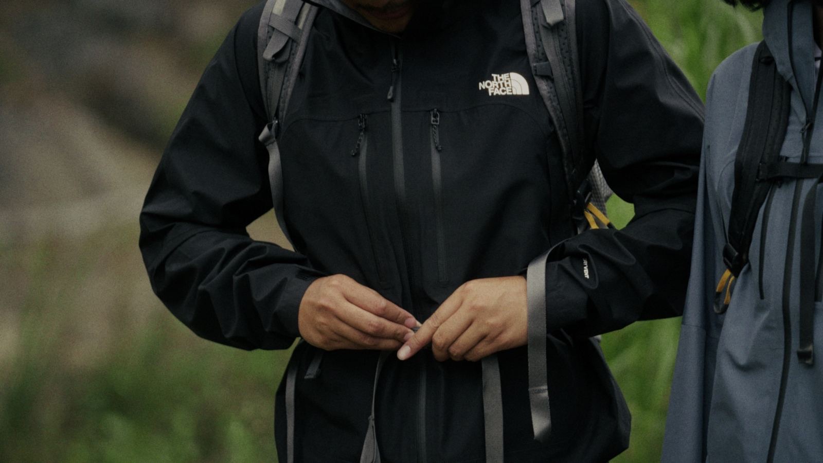 Hands fastening a black shell jacket on the trail